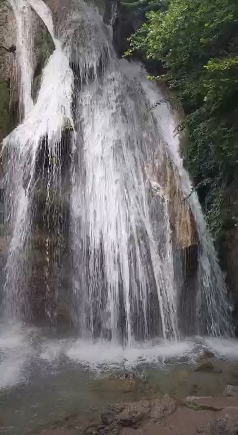 White waterfall among green trees. A clear water waterfall cascades over rocks in a green forest.